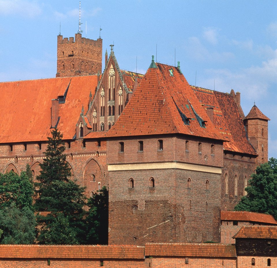 The medieval Malbork Castle with red brick walls and orange roofs surrounded by greenery | MSC Cruises