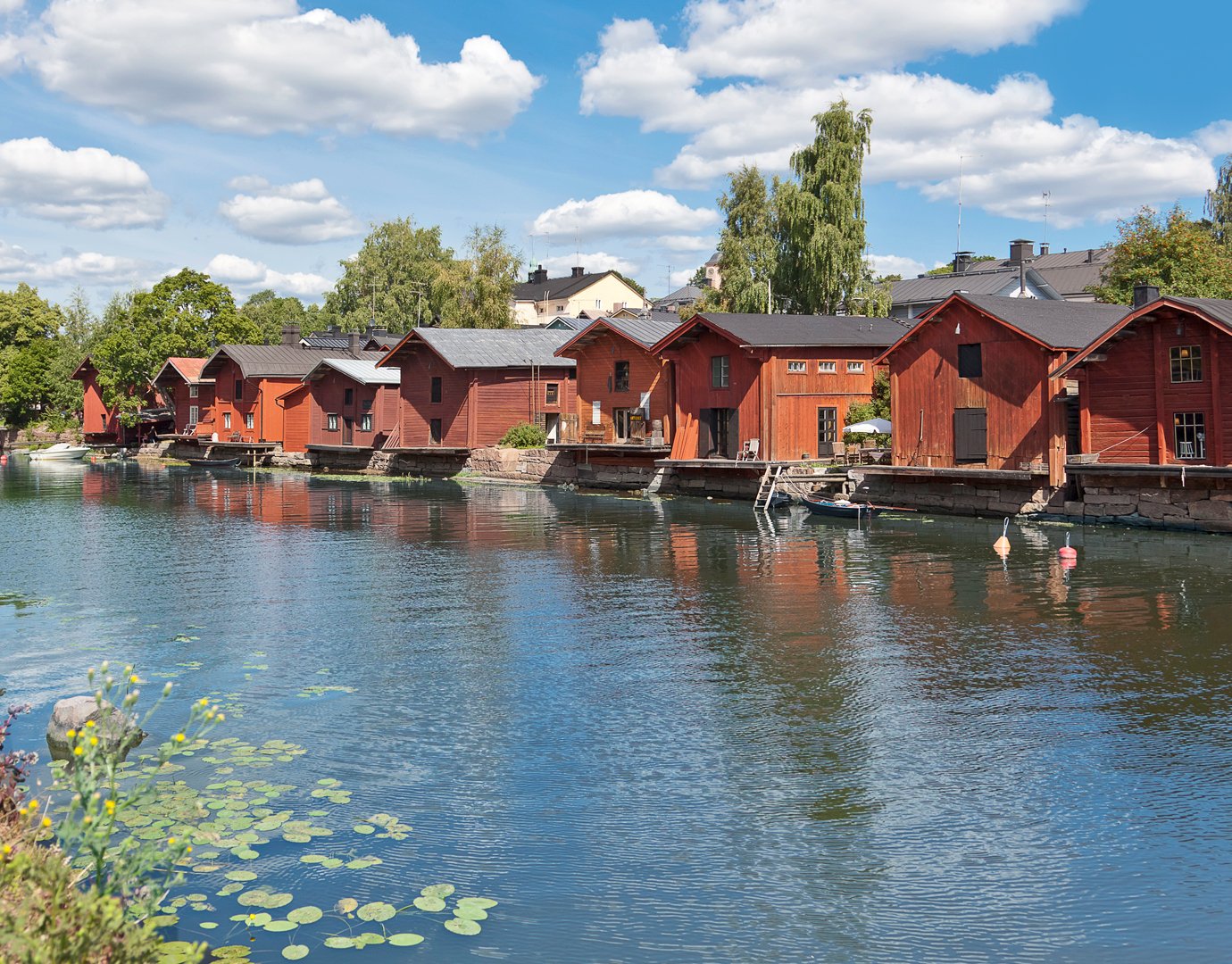Red wooden houses along a calm waterfront with lily pads and blue skies | MSC Cruises