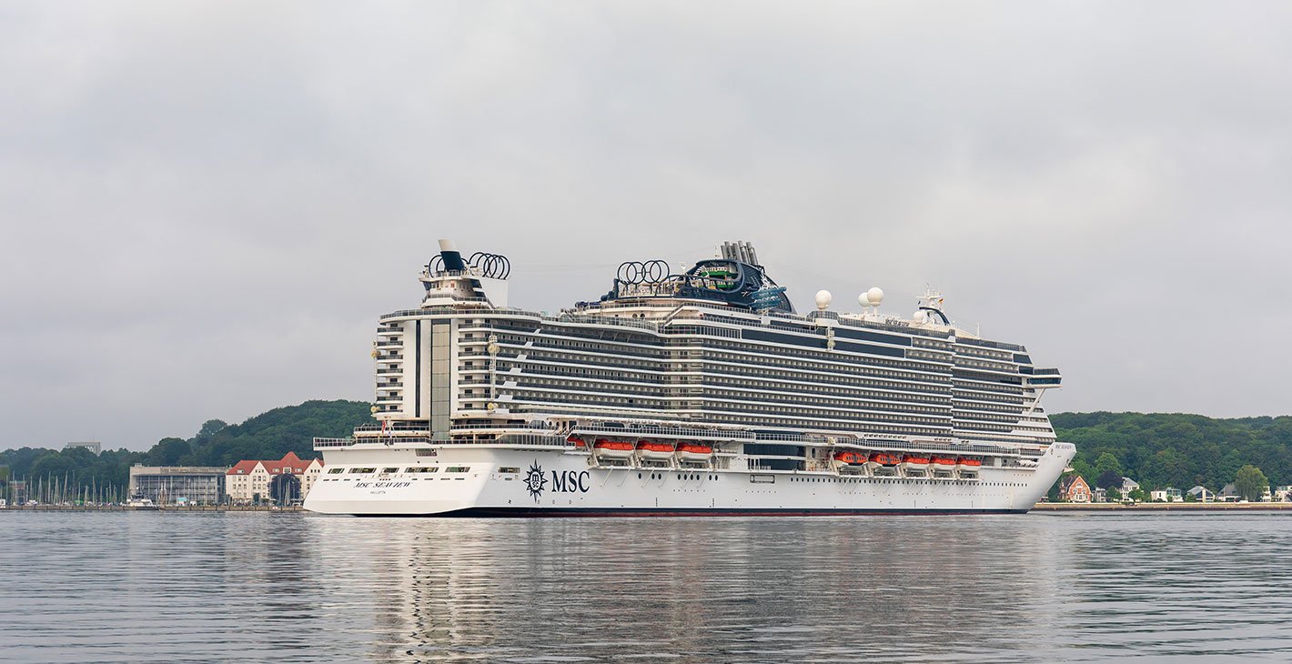 MSC cruise ship docked near a scenic waterfront with lush greenery | MSC Cruises