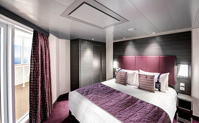Luxurious cruise ship cabin with a king-size bed, elegant decor, and balcony view of the ocean | MSC Cruises
