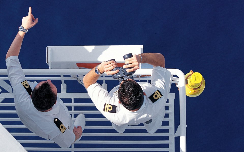 Two uniformed officers on a cruise ship deck, one using binoculars to scan the ocean | MSC Cruises